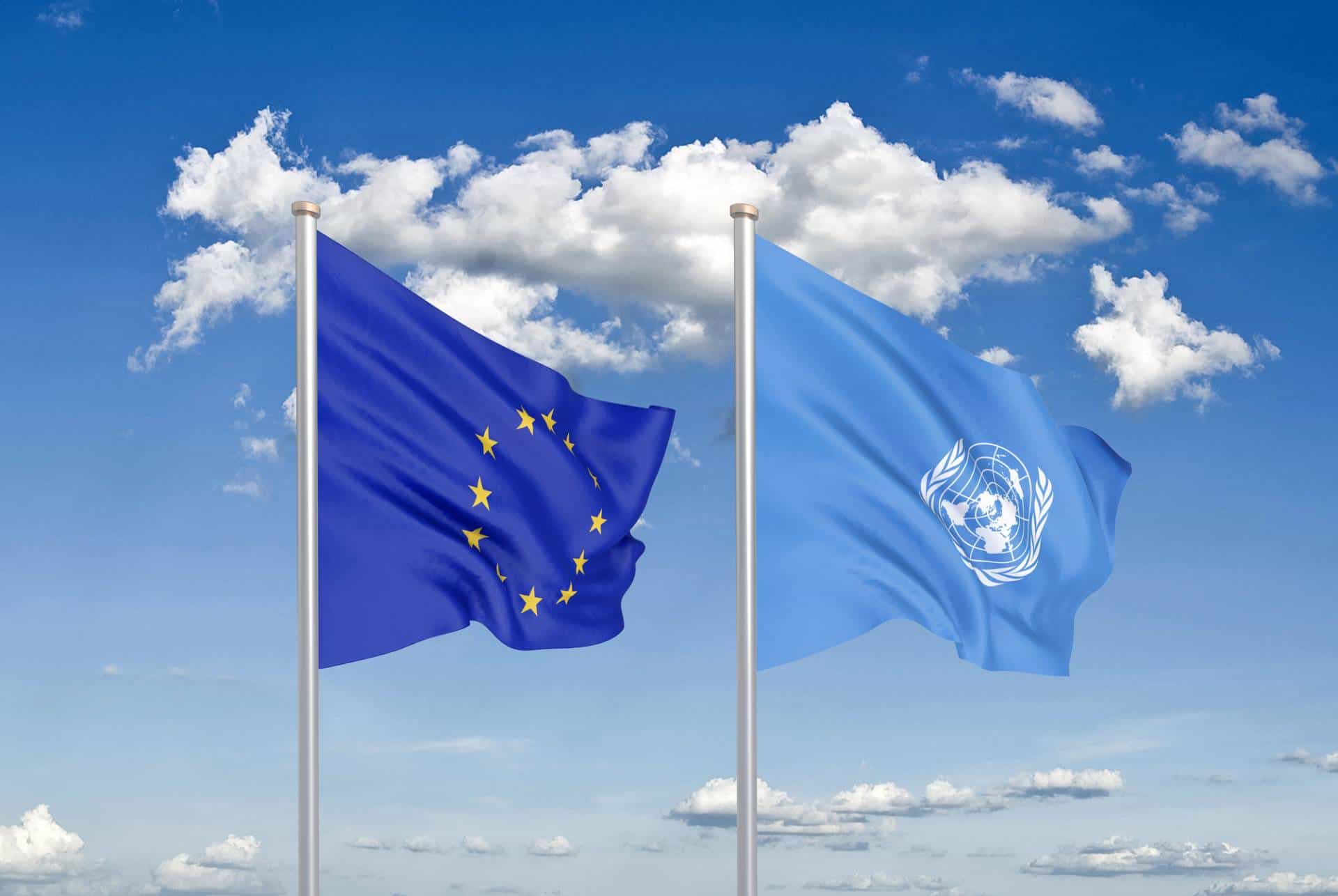 European Union and United Nations flags against blue sky.