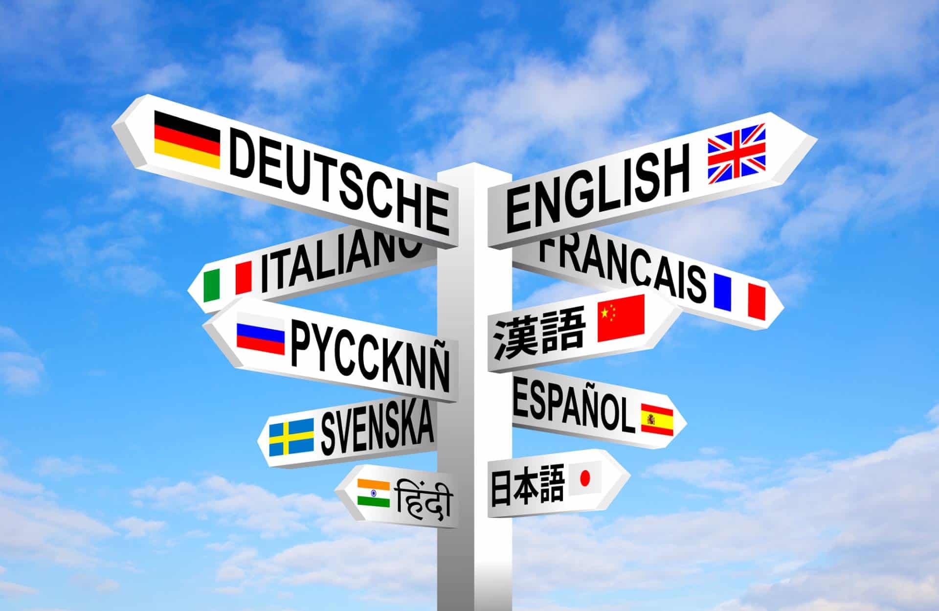 Signpost of different languages and flags against blue sky.
