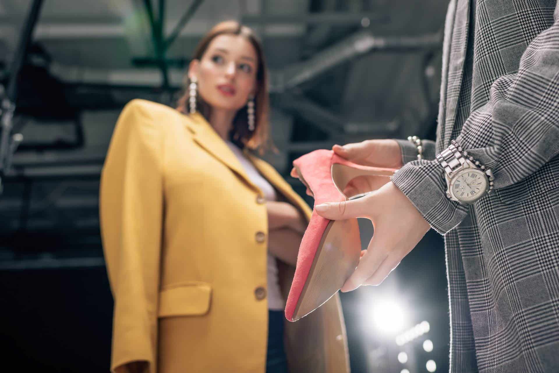 Female stylist holding red shoes near woman wearing oversized yellow suit