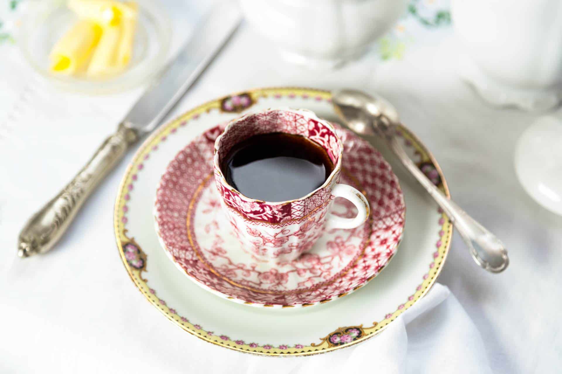 Antique porcelain breakfast setting with coffee on white cloth.