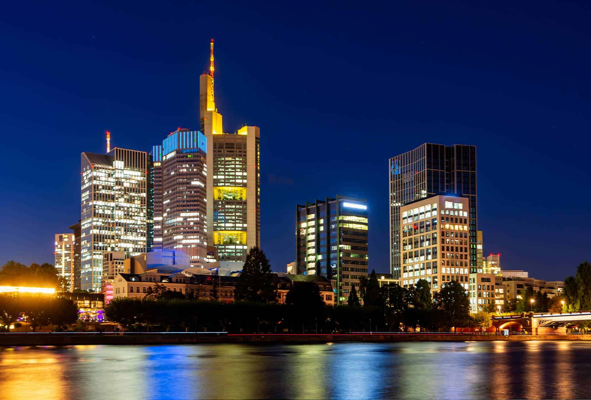 Night view of Frankfurt's skyline from the Main River with the Commerzbank Tower illuminated in yellow lights.