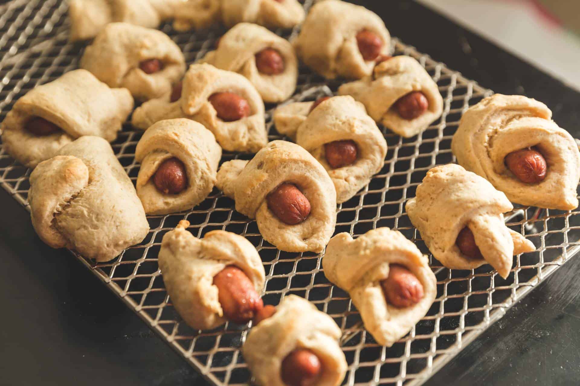 Sausages wrapped in dough and baked also known as "pigs in a blanket" on a metal cooling rack.