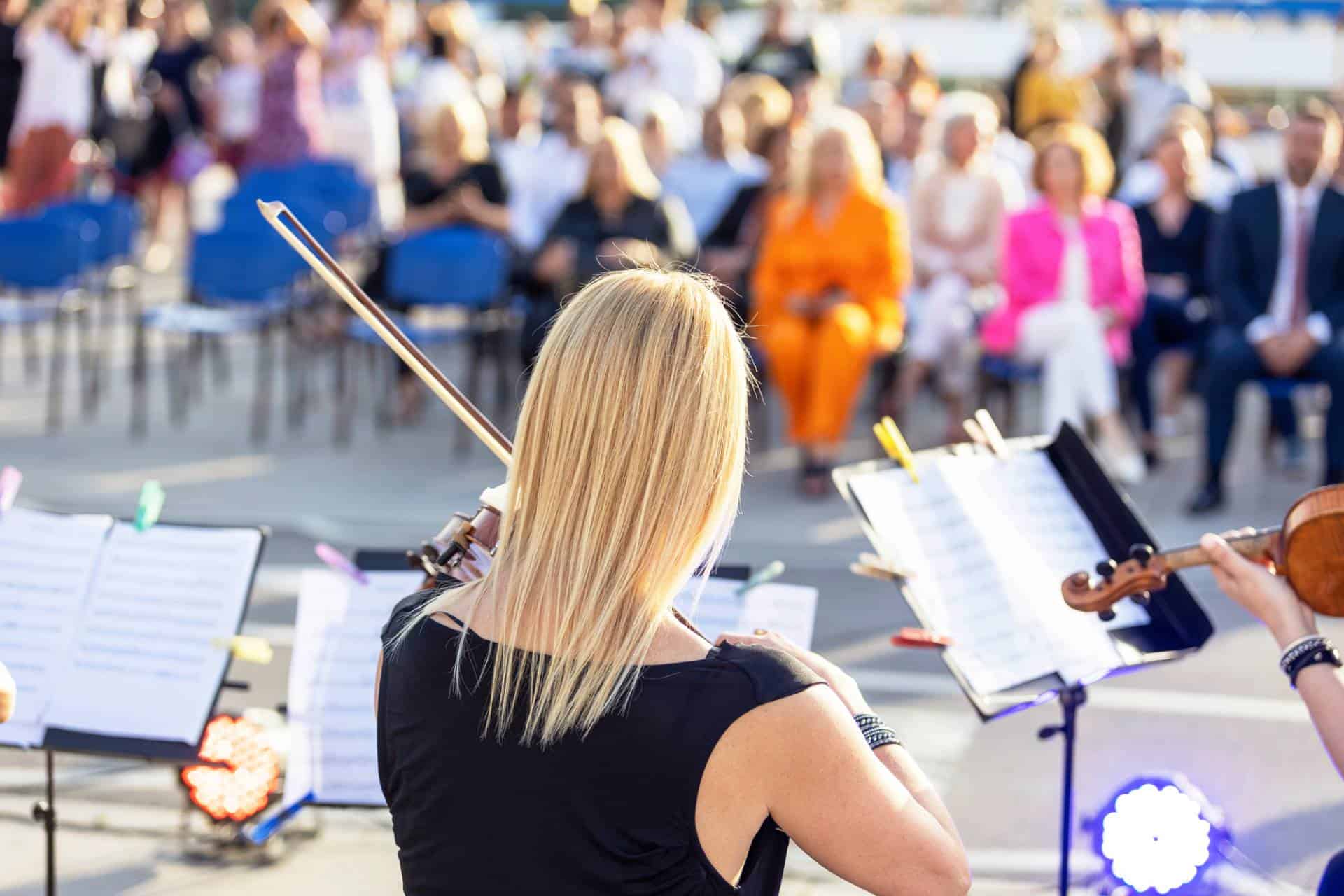 Outdoor classical music concert with audience in the background.
