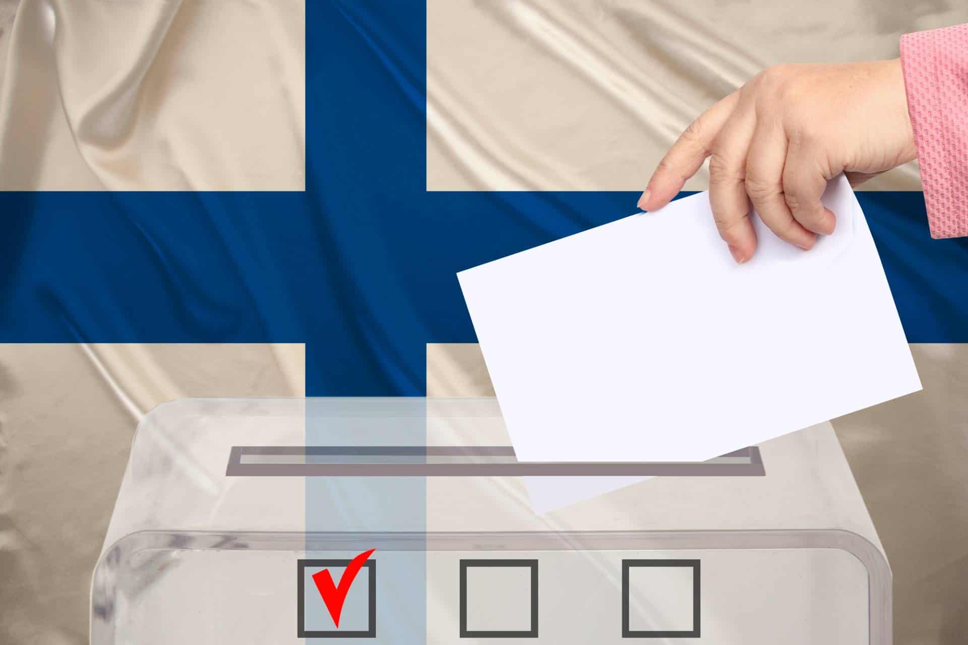 Female voter lowers ballot in a ballot box with Finland's national flag in the background.