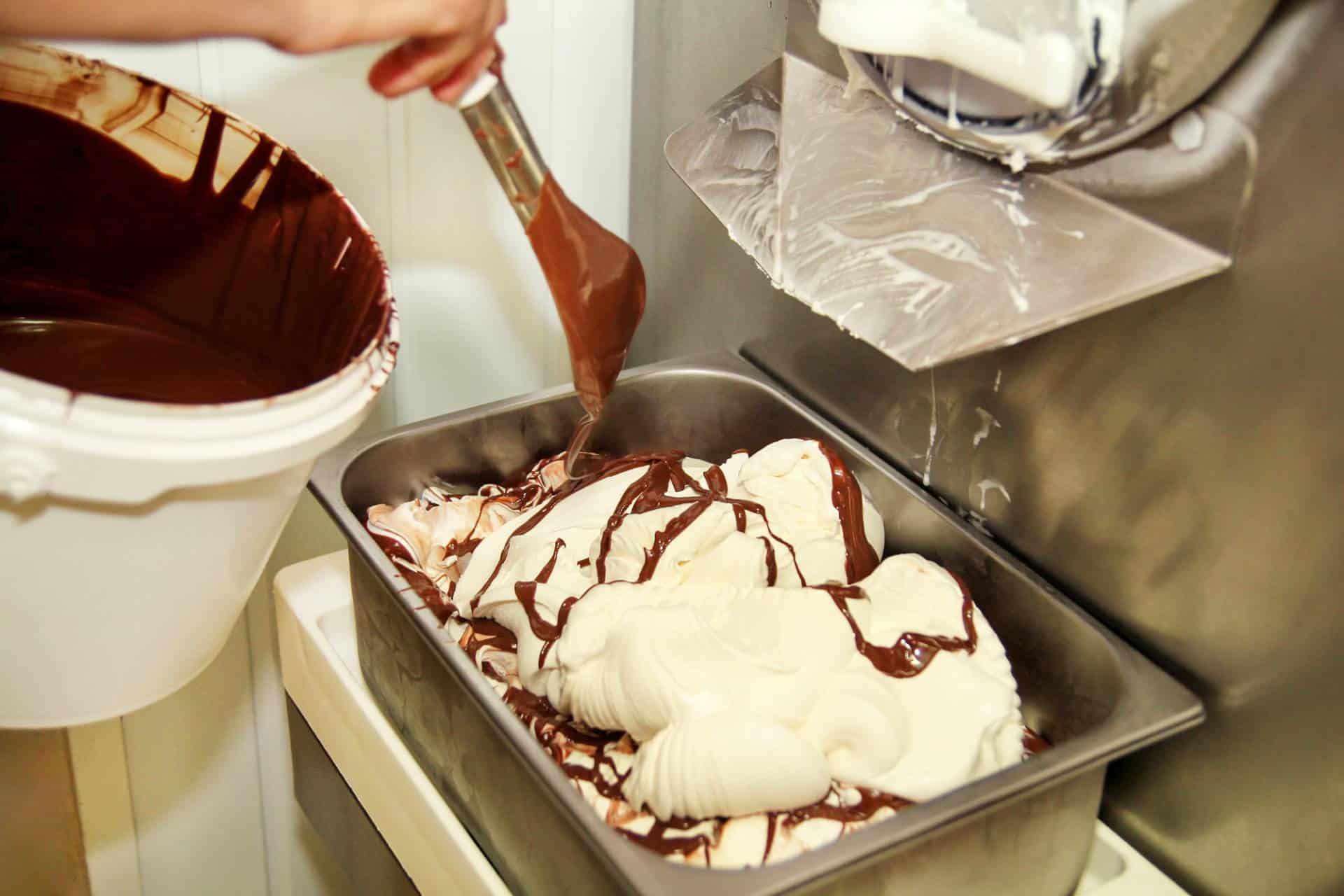 Woman working at ice cream factory adding chocolate swirls to creamy vanilla ice cream.