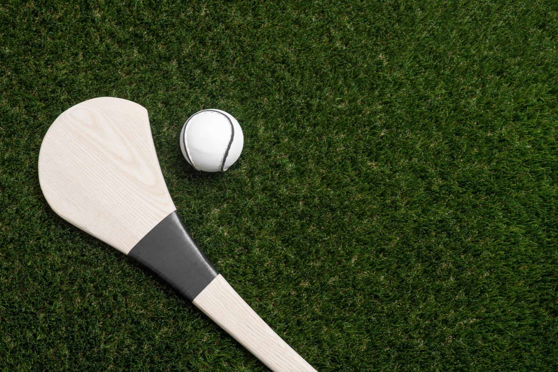Hurling bat and sliotar (a hard leather-covered ball used in the game of hurling) on green grass.
