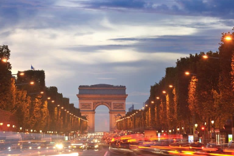 Beautiful night view of Arc de Triomphe in Paris, France with cars and street lights.